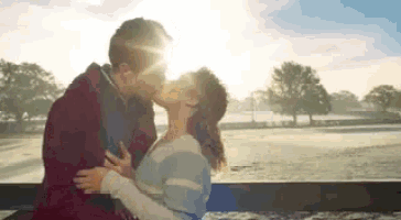 a man and a woman are kissing on a bridge in the sunlight .