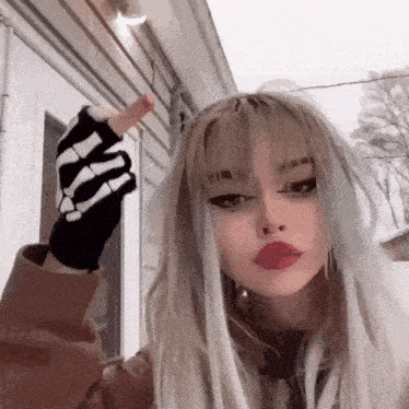a girl with long blonde hair and a skeleton glove on her hand is giving the middle finger .