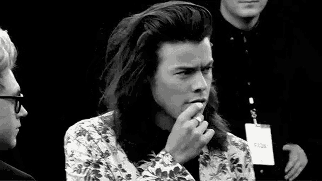 a black and white photo of harry styles smoking a cigarette .