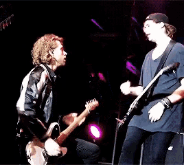 two men are playing guitars on a stage and one of them is wearing a black jacket
