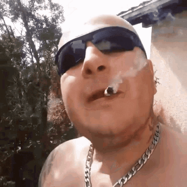a bald man wearing sunglasses and a chain smoking a cigarette