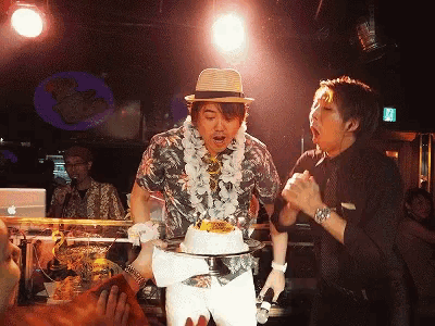 a man in a hawaiian shirt is holding a cake on a stand