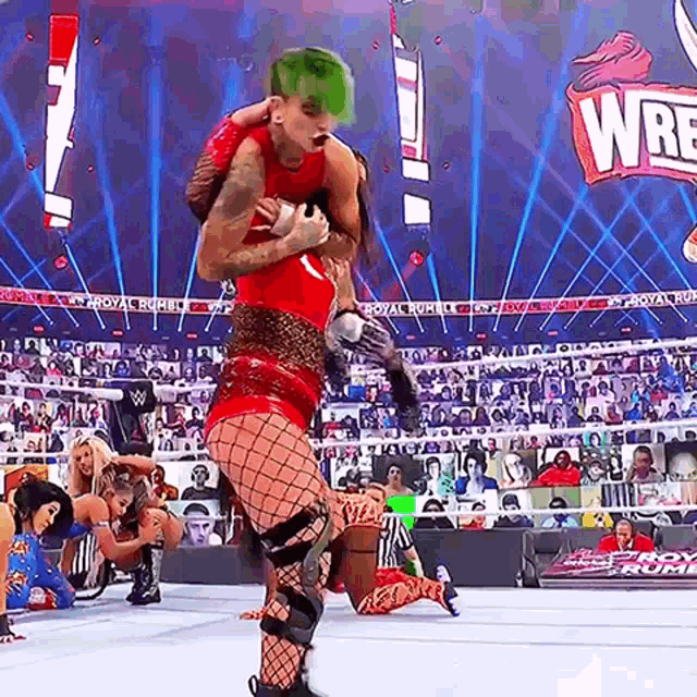 a woman with green hair is wrestling another woman in a wrestling match on a stage .