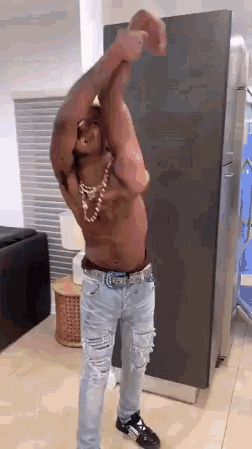 a shirtless man in ripped jeans is standing in front of a refrigerator .