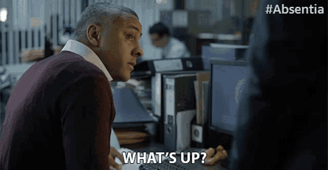 a man sitting at a desk with a computer says what 's up