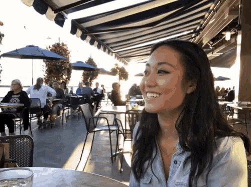 a woman sits at a table with a glass of water and smiles