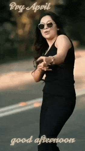 a woman wearing sunglasses and a black dress is dancing on a street .