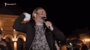 a man with a beard is singing into a microphone in front of a crowd at night .
