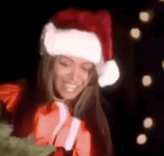 a woman in a santa hat is holding a christmas tree and smiling .