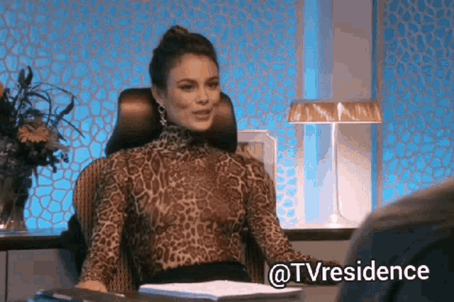 a woman in a leopard print top is sitting at a desk