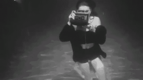 a black and white photo of a woman taking a picture underwater