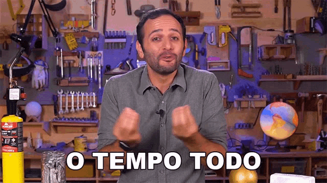 a man in a gray shirt says o tempo todo in front of a workbench