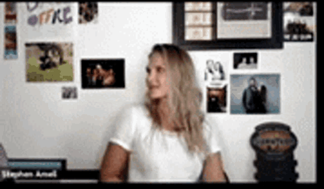 a woman in a white shirt is sitting in front of a wall with pictures and a sign that says office