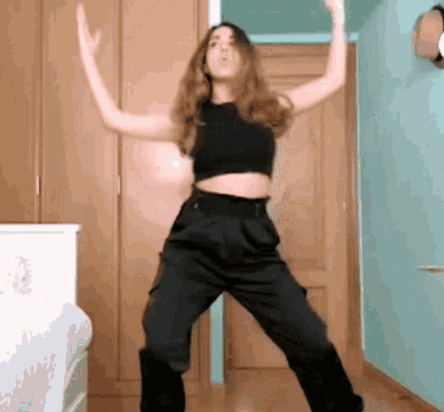 a woman in a crop top and black pants is dancing in a bedroom .