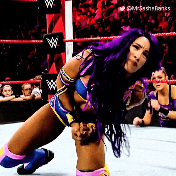a female wrestler with purple hair is kneeling down in a wrestling ring .