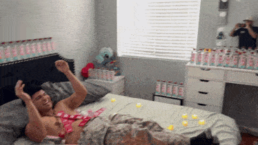 a shirtless man is laying on a bed with bottles of water behind him