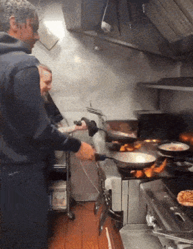 two men are cooking in a kitchen and one is holding a frying pan
