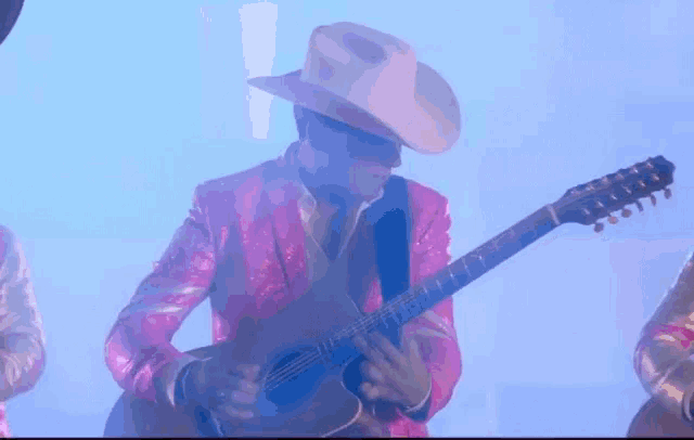a man in a cowboy hat is playing a guitar in a pink jacket .