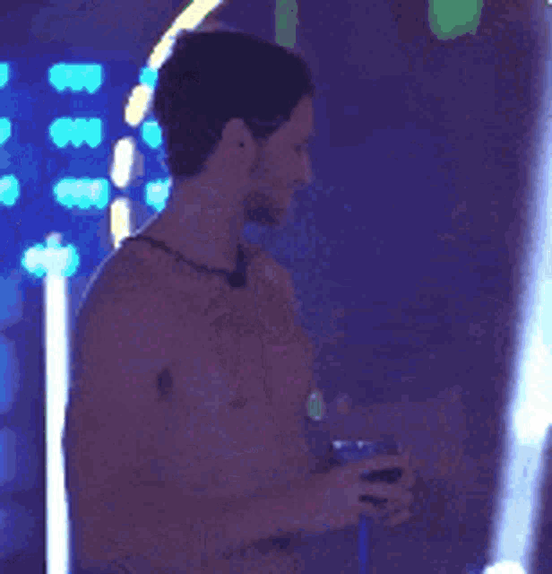 a man without a shirt is standing in a dark room holding a glass