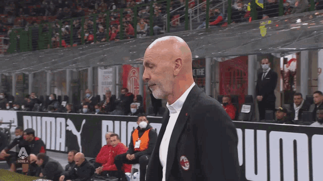 a bald man stands in front of a puma banner
