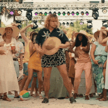 a group of people are dancing on a beach with a man holding a hat