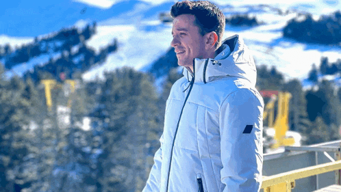 a man in a white jacket is standing in front of a snow covered mountain .