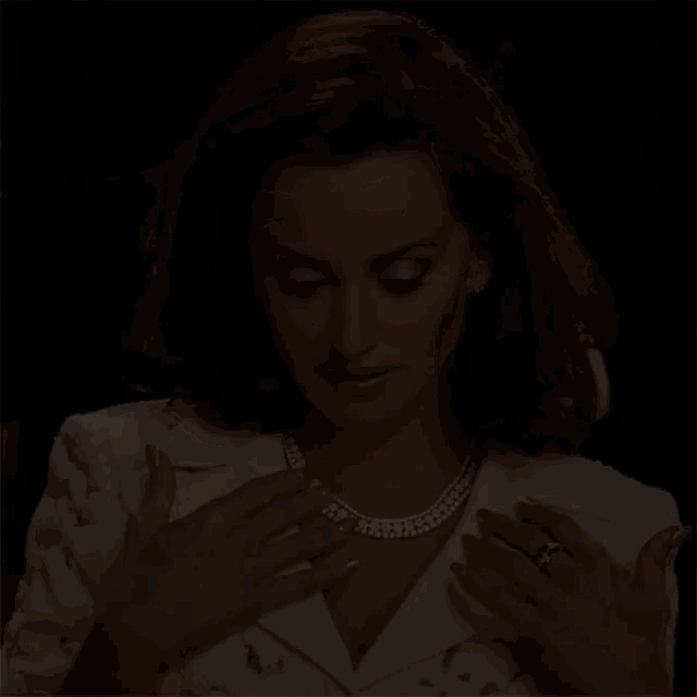 a woman in a white jacket and pearl necklace