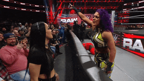 a woman with purple hair stands next to another woman in front of a crowd at a raw event