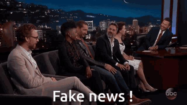 a group of people are sitting in front of a table with fake news written on it