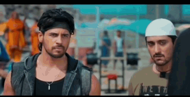 two men are standing next to each other on a beach and one of them is wearing a headband .