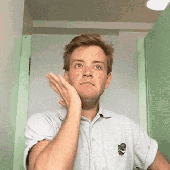 a man in a gray shirt is making a funny face while standing in front of a green door .