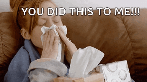 a woman blowing her nose with a box of tissues in front of her