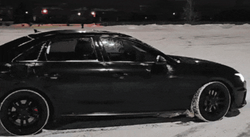 a black car is parked in a snowy parking lot at night