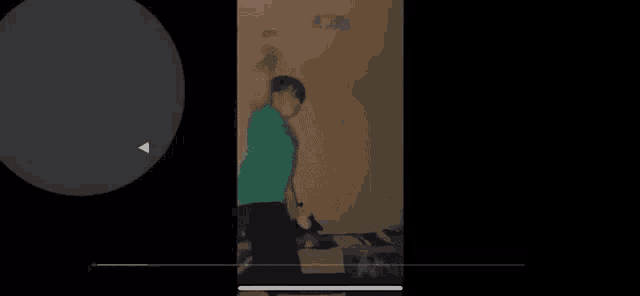 a man in a green shirt is dancing in a dark room with a black background .