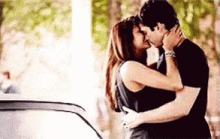 a man and a woman are kissing while standing next to a car .