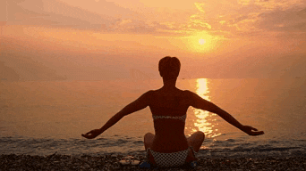 a woman in a bikini sits on the beach with her arms outstretched