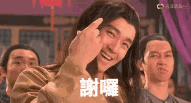 a man with long hair is giving the middle finger in front of a crowd of people .