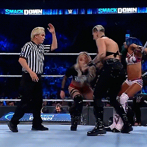 a referee stands in the middle of a wrestling match with a smack down sign behind him