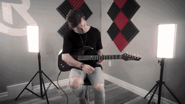 a man playing a guitar in a room with a r on the wall