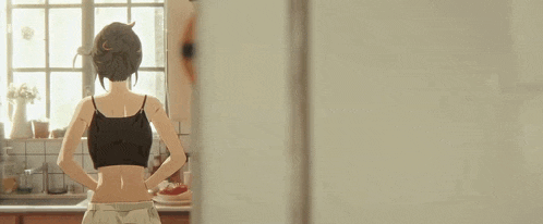 a woman is standing in a kitchen with her hands on her hips and looking out the window .