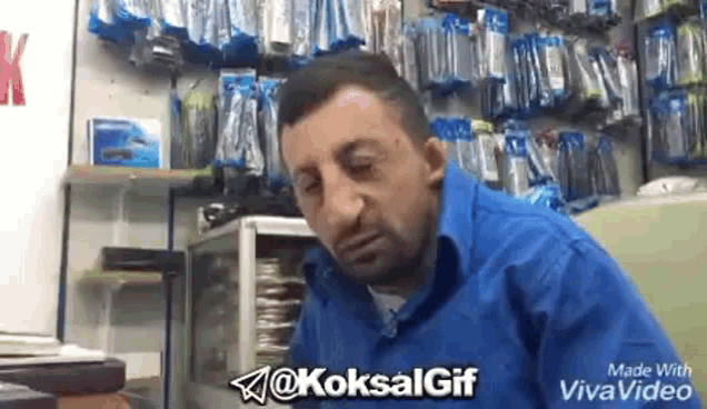 a man in a blue shirt is sitting at a table in a store with a beard .