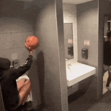 a person holding a basketball in a bathroom with a sign that says " no smoking "