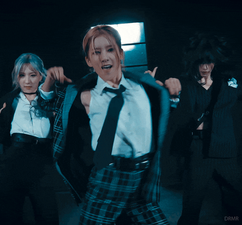 a woman in a plaid suit and tie is dancing in a dark room with drmr written on the bottom