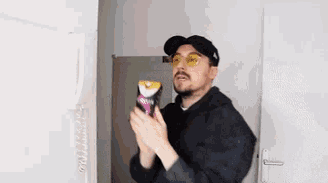 a man wearing sunglasses and a hat is holding a bag of chips in his hands .