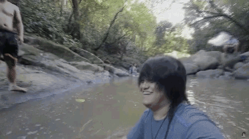 a man in a blue shirt is standing in a river smiling