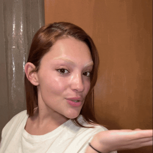 a woman with red hair is wearing a white shirt and holding her hand out