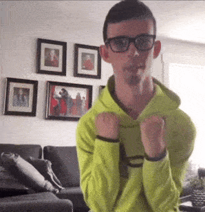a young man wearing glasses and a neon green hoodie is standing in a living room .