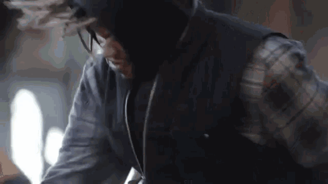 a man wearing a hooded jacket and glasses is smoking a cigarette .