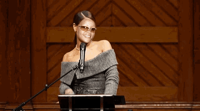 a woman wearing sunglasses is standing at a podium with a microphone in front of her