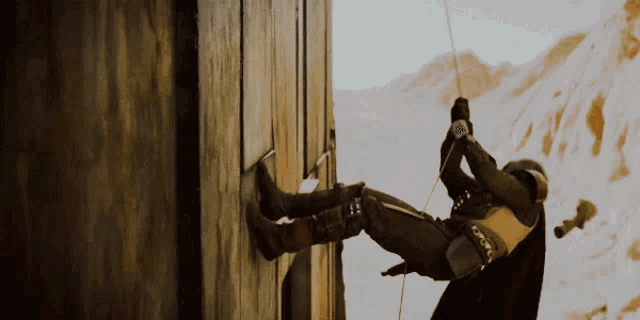 a man is climbing up a wooden wall with a rope attached to him